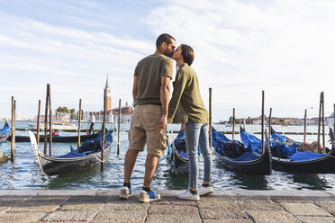 Italy, Venice, affectionate young couple kissing with gondola boats in background - WPEF01251