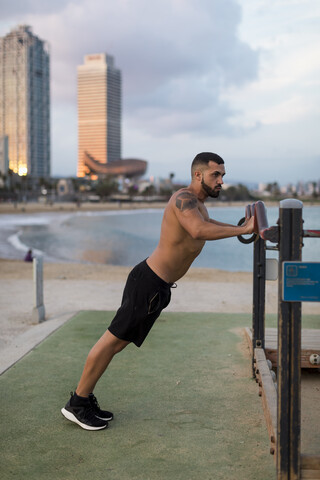 Muskulöser Mann mit nacktem Oberkörper beim Workout am Strand, lizenzfreies Stockfoto