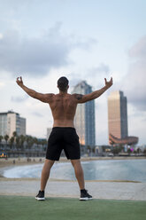 Barechested muscular man posing on the beach at dusk - MAUF02220