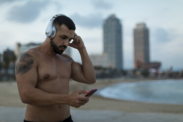 Barechested muscular man with headphones and cell phone outdoors - MAUF02231