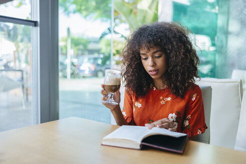 Porträt einer jungen Frau, die in einem Café Kaffee trinkt und ein Buch liest - KIJF02136