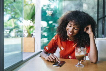 Portrait of smiling young woman in coffee shop using cell phone - KIJF02142