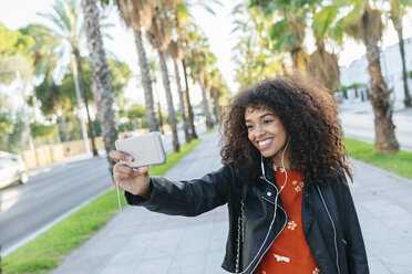 Porträt einer lächelnden jungen Frau, die ein Selfie mit ihrem Smartphone macht - KIJF02160