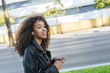 Portrait of smiling young woman listening music with earphones and smartphone - KIJF02161