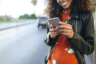 Frau steht am Straßenrand und hält ein Smartphone, Nahaufnahme - KIJF02168