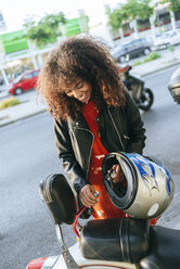 Lächelnde junge Frau beim Entfernen des Sicherheitsschlosses von ihrem Motorrad - KIJF02170