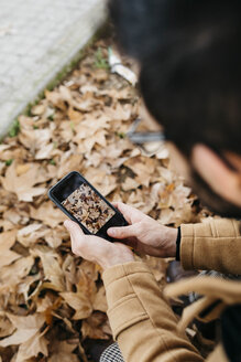 Nahaufnahme eines Mannes, der mit seinem Handy ein Foto von Herbstblättern macht - JRFF02298
