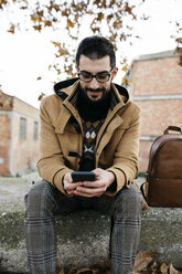 Spanien, Igualada, lächelnder Mann sitzt und telefoniert in der herbstlichen Stadt - JRFF02301
