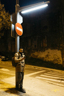 Spanien, Igualada, Mann steht nachts unter einer Straßenlaterne und benutzt ein Mobiltelefon - JRFF02316