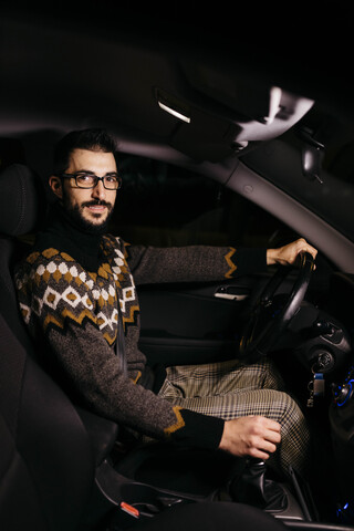 Porträt eines selbstbewussten Mannes am Steuer eines Autos bei Nacht, lizenzfreies Stockfoto