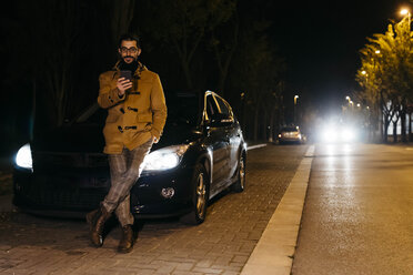 Spanien, Igualada, Mann benutzt Handy außerhalb des Autos bei Nacht - JRFF02328