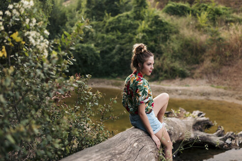 Young woman sitting on a trunk surrounded by nature - LOTF00022