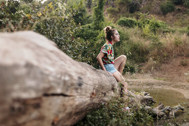 Junge Frau sitzt auf einem Baumstamm, umgeben von Natur - LOTF00023