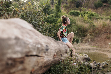 Young woman sitting on a trunk surrounded by nature - LOTF00023