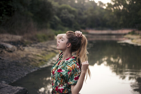 Young woman touching her hair next to a lake - LOTF00028