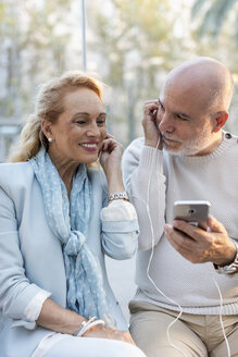 Spanien, Barcelona, glückliches älteres Paar, das sich ein Smartphone mit Kopfhörern teilt - MAUF02242