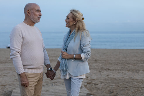 Spanien, Barcelona, glückliches älteres Paar Hand in Hand am Strand in der Abenddämmerung - MAUF02259