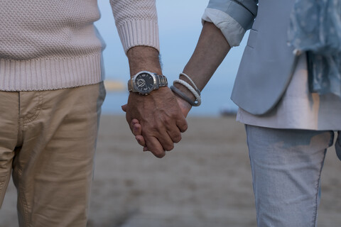 Nahaufnahme eines älteren Paares Hand in Hand am Strand in der Abenddämmerung, lizenzfreies Stockfoto