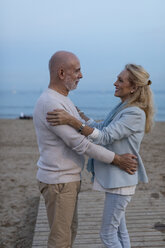 Spanien, Barcelona, glückliches älteres Paar, das sich am Strand in der Abenddämmerung umarmt - MAUF02261