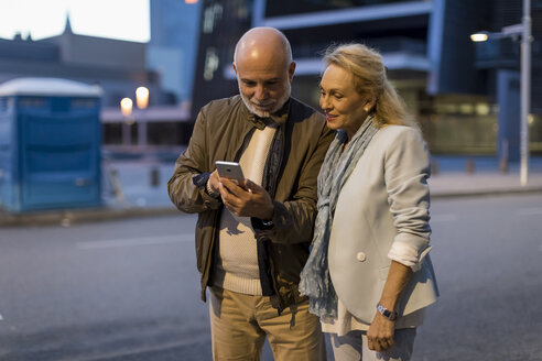 Spanien, Barcelona, älteres Paar, das in der Abenddämmerung in der Stadt ein Handy benutzt - MAUF02266
