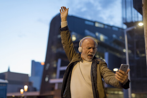 Spain, Barcelona, excited senior man with headphones and cell phone in the city at dusk stock photo