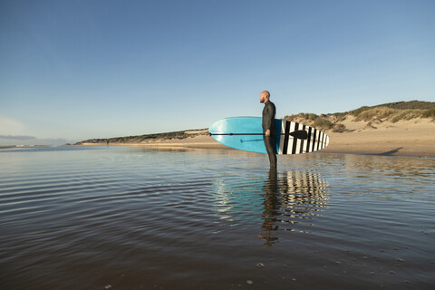 Spanien, Andalusien, Tarifa, Mann hält Stand Up Paddle Board im Meer, lizenzfreies Stockfoto