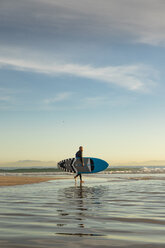 Spain, Andalusia, Tarifa, man walking with stand up paddle board on the beach - KBF00359