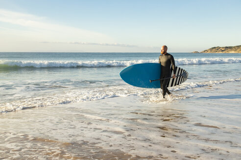 Spanien, Andalusien, Tarifa, Mann zu Fuß mit Stand Up Paddle Board am Meer - KBF00367