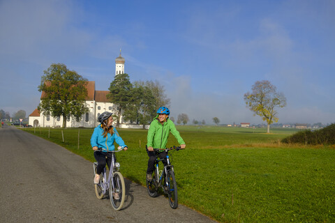 Deutschland, Wallfahrtskirche St. Coloman und Radlerpaar auf Tour, lizenzfreies Stockfoto