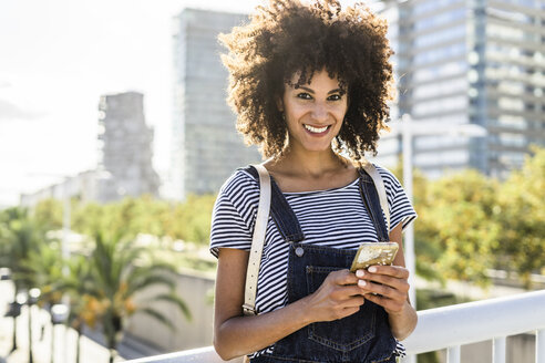 Junge Frau steht auf einer Brücke und hält ein Smartphone in der Hand - GIOF05336