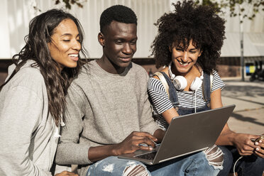 Freunde sitzen auf einer Bank in der Stadt, haben Spaß, benutzen einen Laptop - GIOF05379