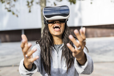 Junge Frau benutzt VR-Brille in der Stadt und streckt die Hand aus - GIOF05389