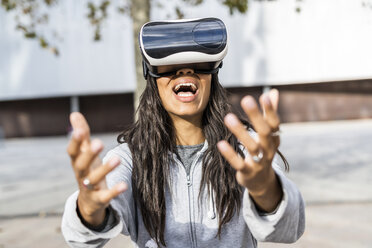 Young woman using VR goggles in the city, reaching out - GIOF05389