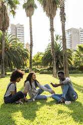 Friends sitting on grass, having fun, using smartphone - GIOF05404