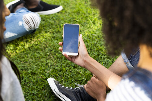 Junge Frau verbringt ihre Zeit mit Freunden in einem Park und hält ihr Smartphone in der Hand - GIOF05410