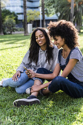 Freundinnen sitzen im Park, haben Spaß, benutzen Smartphone - GIOF05418