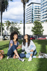 Girlfriends sitting in park, having fun, using smartphone - GIOF05421