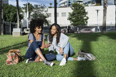 Girlfriends sitting in park, having fun, using smartphone - GIOF05422