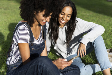 Girlfriends sitting in park, having fun, using smartphone - GIOF05423