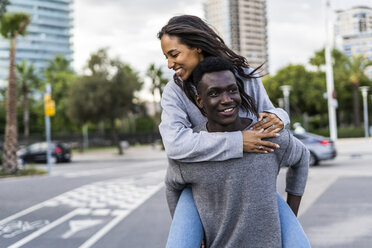 Young man carrying his girlfriend piggyback in the street - GIOF05434