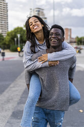 Young man carrying his girlfriend piggyback in the street - GIOF05435