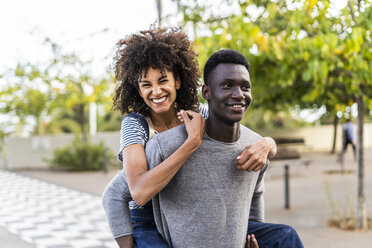 Young man carrying his girlfriend piggyback in the street - GIOF05436