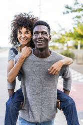 Young man carrying his girlfriend piggyback in the street - GIOF05438