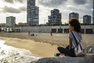 Young woman relaxing on the beach, sitting on rocks, rear view - GIOF05446