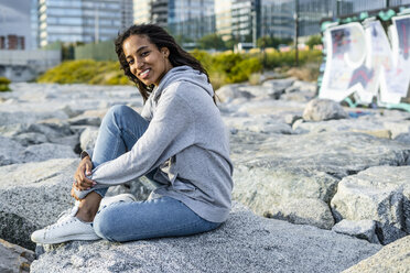 Junge Frau sitzt auf Felsen am Strand und entspannt sich - GIOF05449