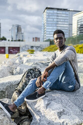 Young man sitting on rocks at the beach, relaxing - GIOF05450