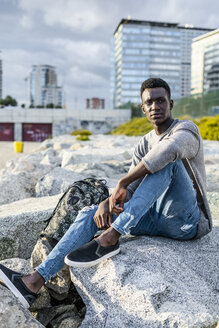 Junger Mann sitzt auf Felsen am Strand und entspannt sich - GIOF05450