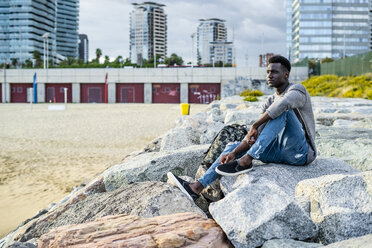 Junger Mann sitzt auf Felsen am Strand und entspannt sich - GIOF05451