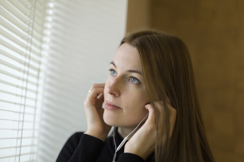 Porträt einer Frau am Fenster, die sich einen Kopfhörer aufsetzt, lizenzfreies Stockfoto