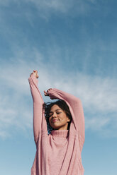 Porträt einer lächelnden jungen Frau mit rosa Pullover gegen den Himmel - LOTF00032